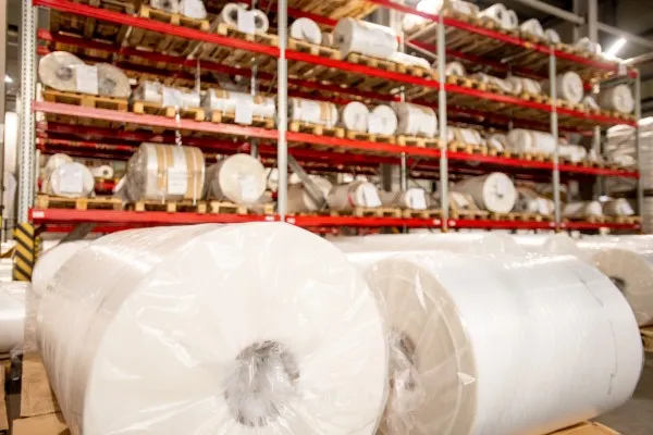 Rollos de película de polietileno blanco empacados y organizados sobre racks selectivos en un almacén para un almacenamiento eficiente.
